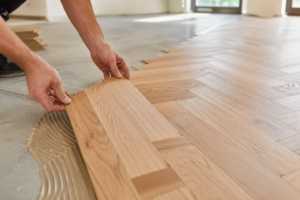 Handwerker verlegt Parkettboden in einem leeren hellen Zimmer in Neunkirchen